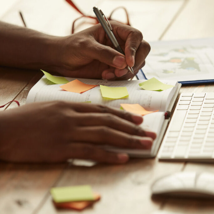 Cropped photo of afro american businessman making some notes while working remotely at home. Male hands taking notes. Freelance. Home office workplace
